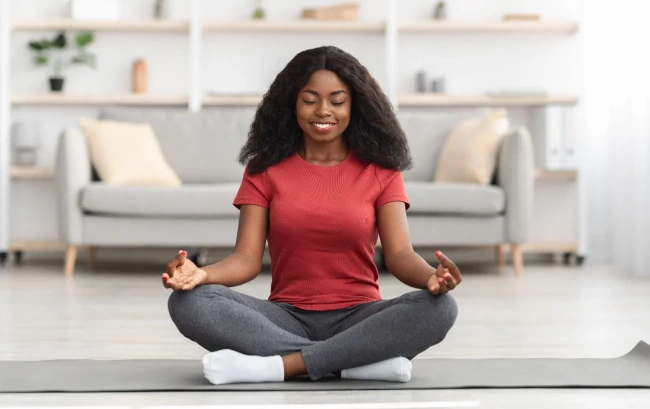 Black woman meditating at home, representing healthy lifestyle and behavioral weight management